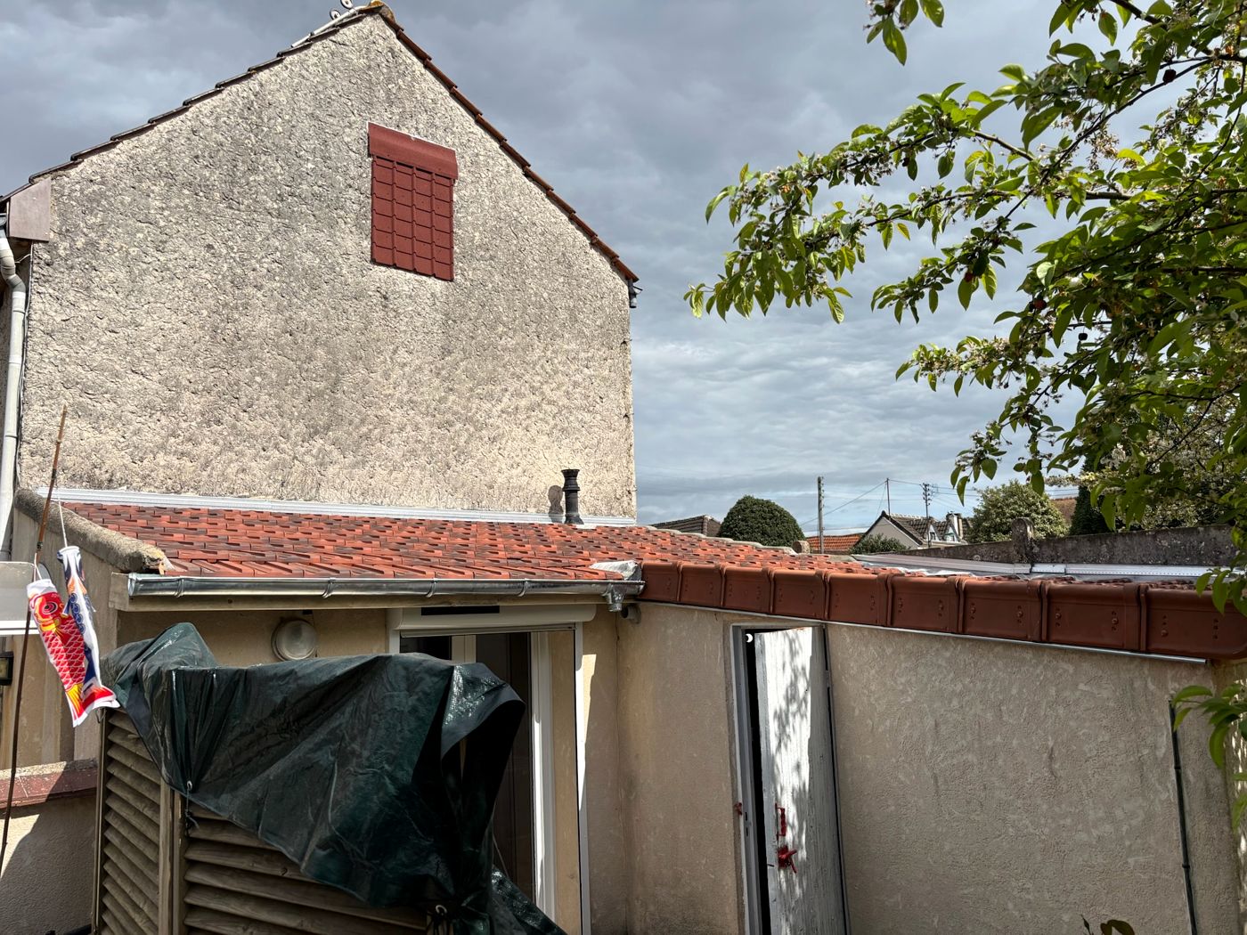 Toiture de l'extension recouverte de tuiles neuves avec sa gouttière, sous le pignon de la maison