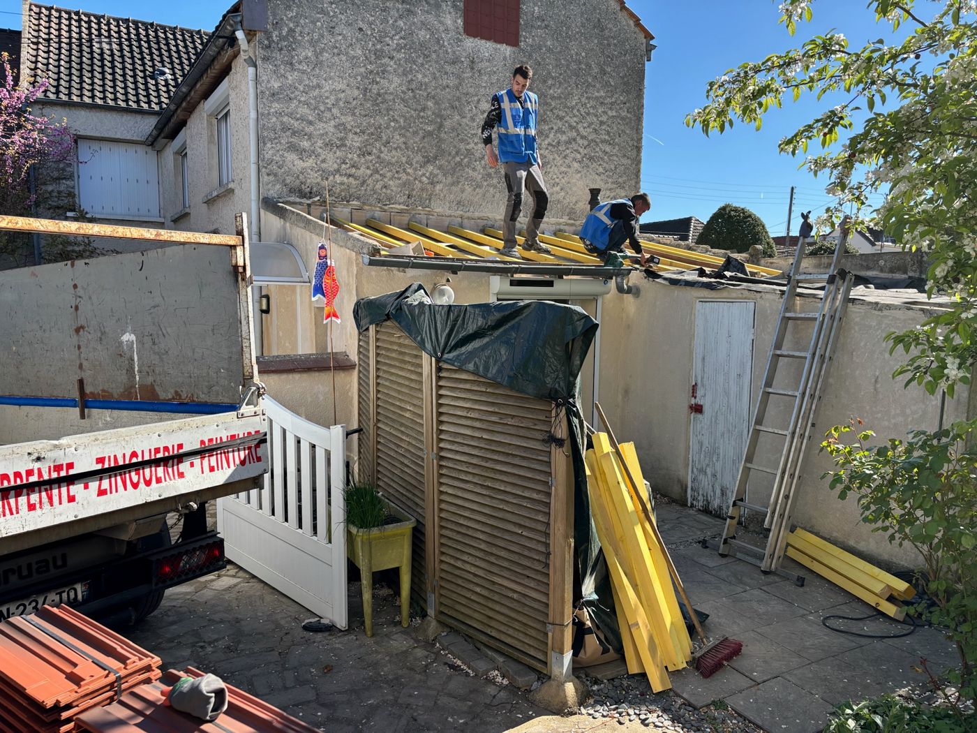 Deux couvreurs fixent des liteaux neufs sur la toiture de l'extension, côté cour, à La Norville