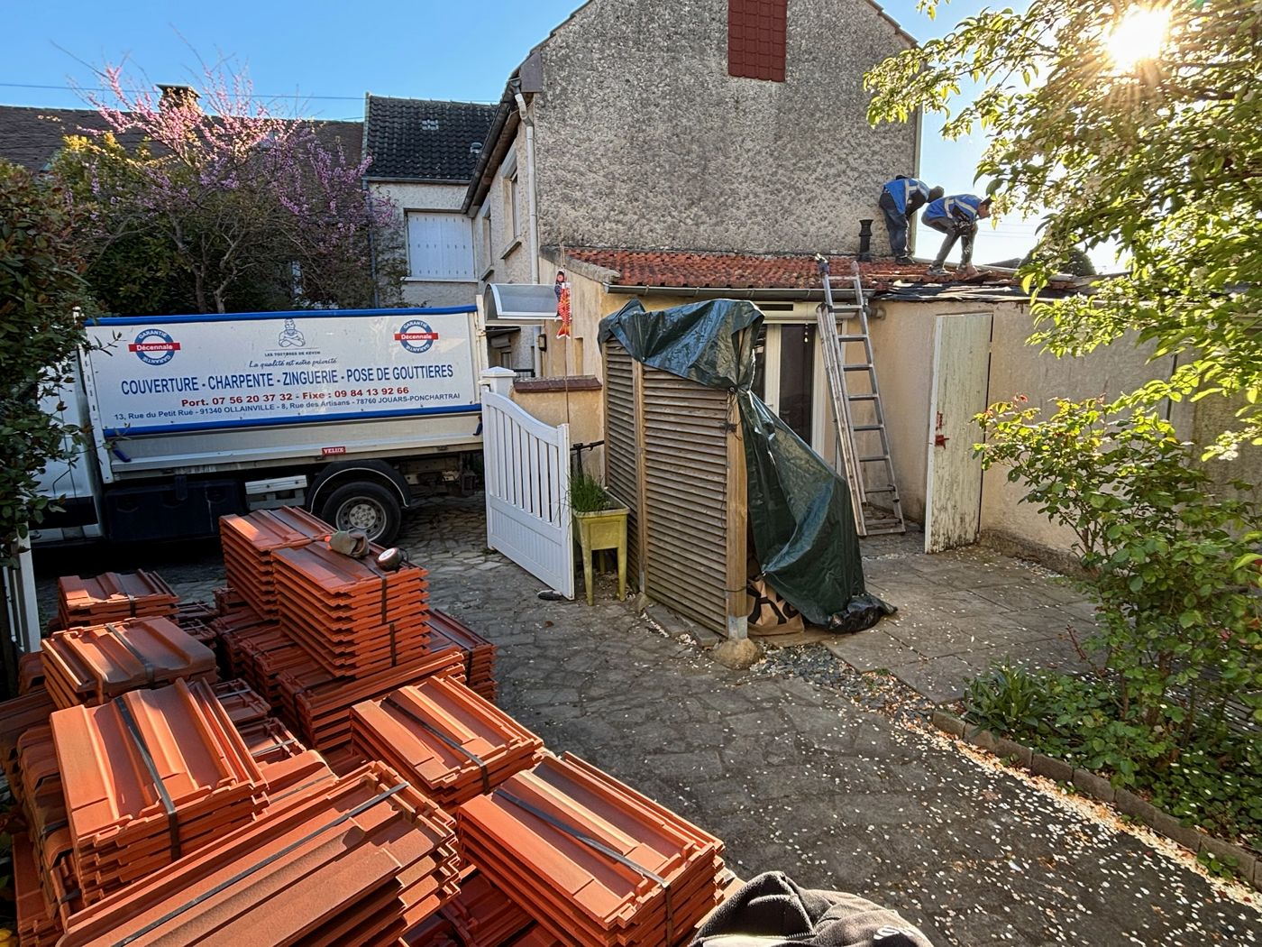 Palettes de tuiles neuves dans la cour et deux couvreurs sur la toiture de l'extension à La Norville