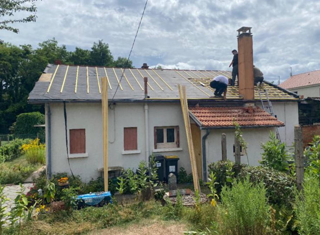 Couvreurs en train de liteauner une toiture autour de la souche de cheminée